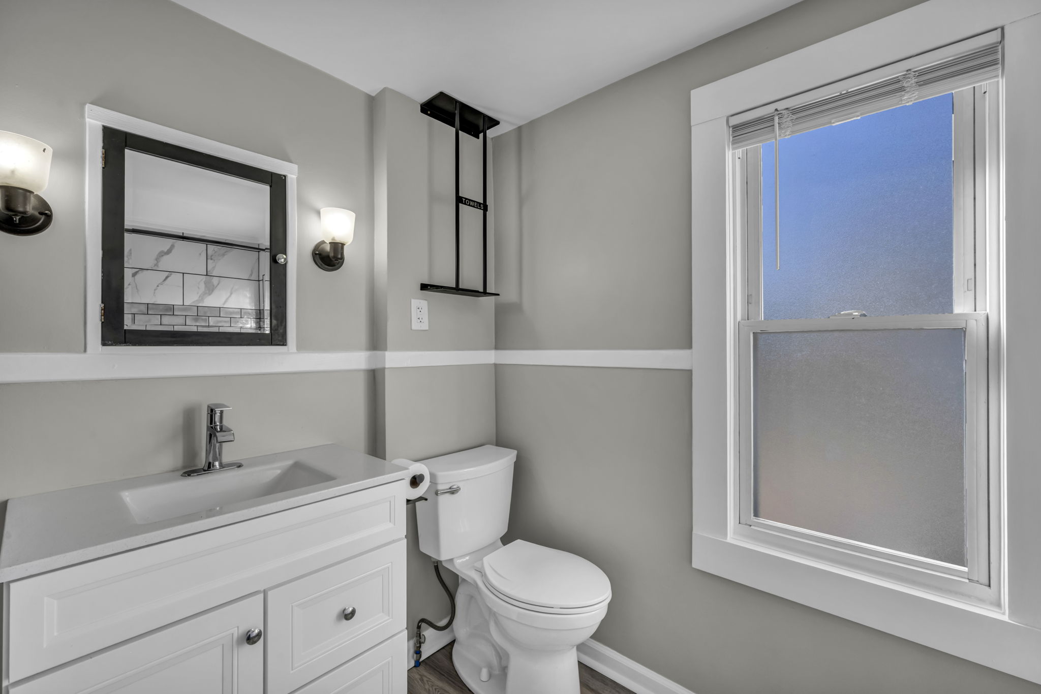 bathroom with vanity, with black bordered mirror above sink, toilet, with oversized window next to it