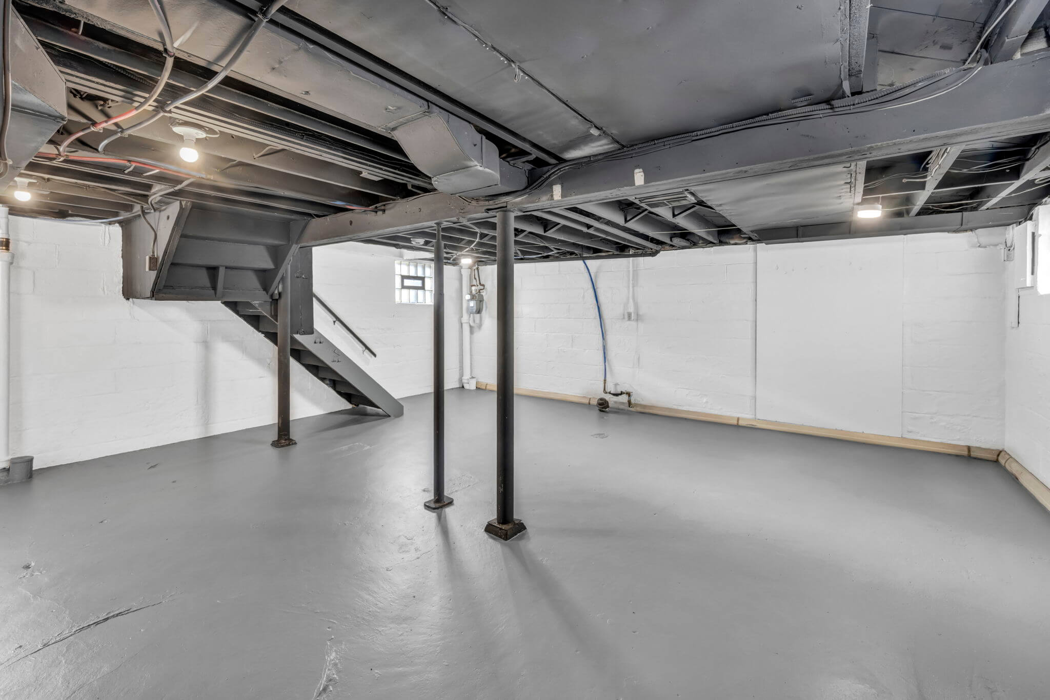 basement photo white walls grey painted floor and charcoal painted ceilings with stairs in the background