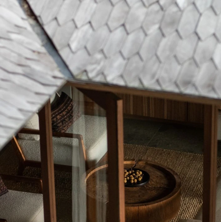 Detail of a shingled roof and window revealing a seating area inside a timber interior.
