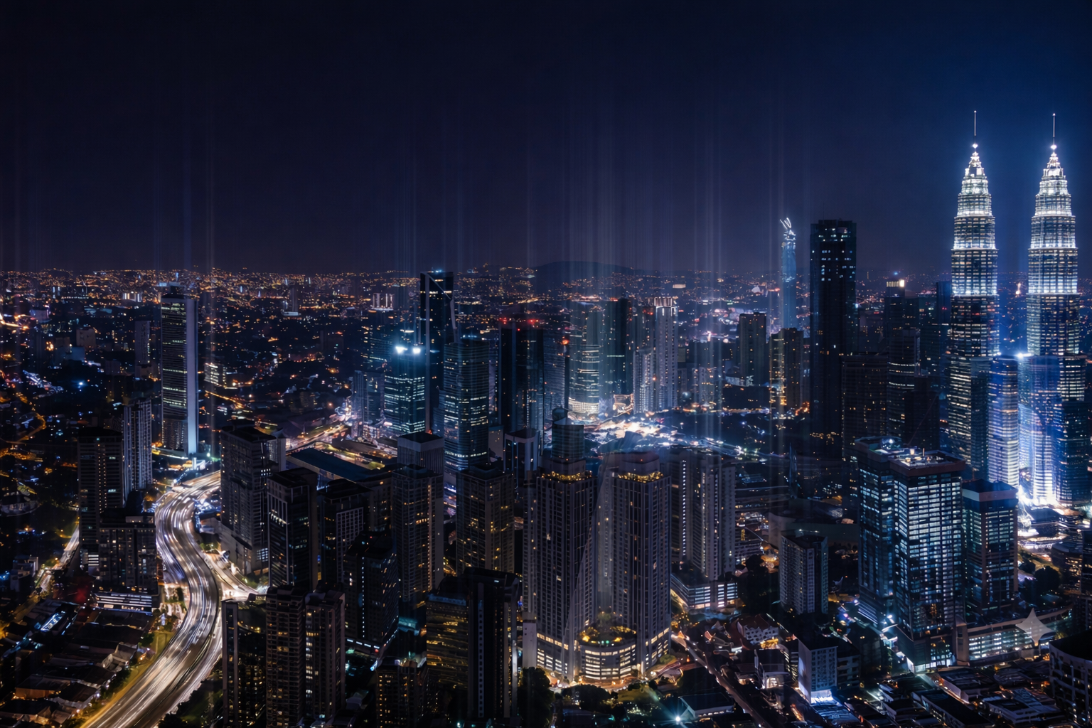 Nighttime cityscape with illuminated skyscrapers and busy light trails on a curved highway.