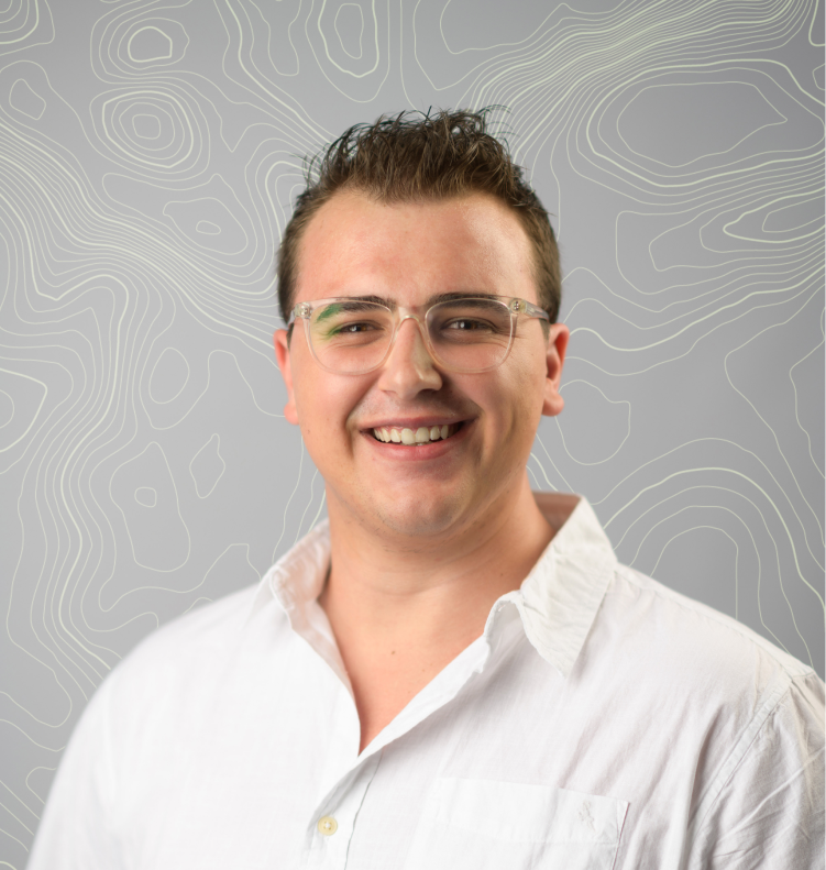 Smiling man with short dark hair, glasses, and white shirt against a gray background with line patterns.