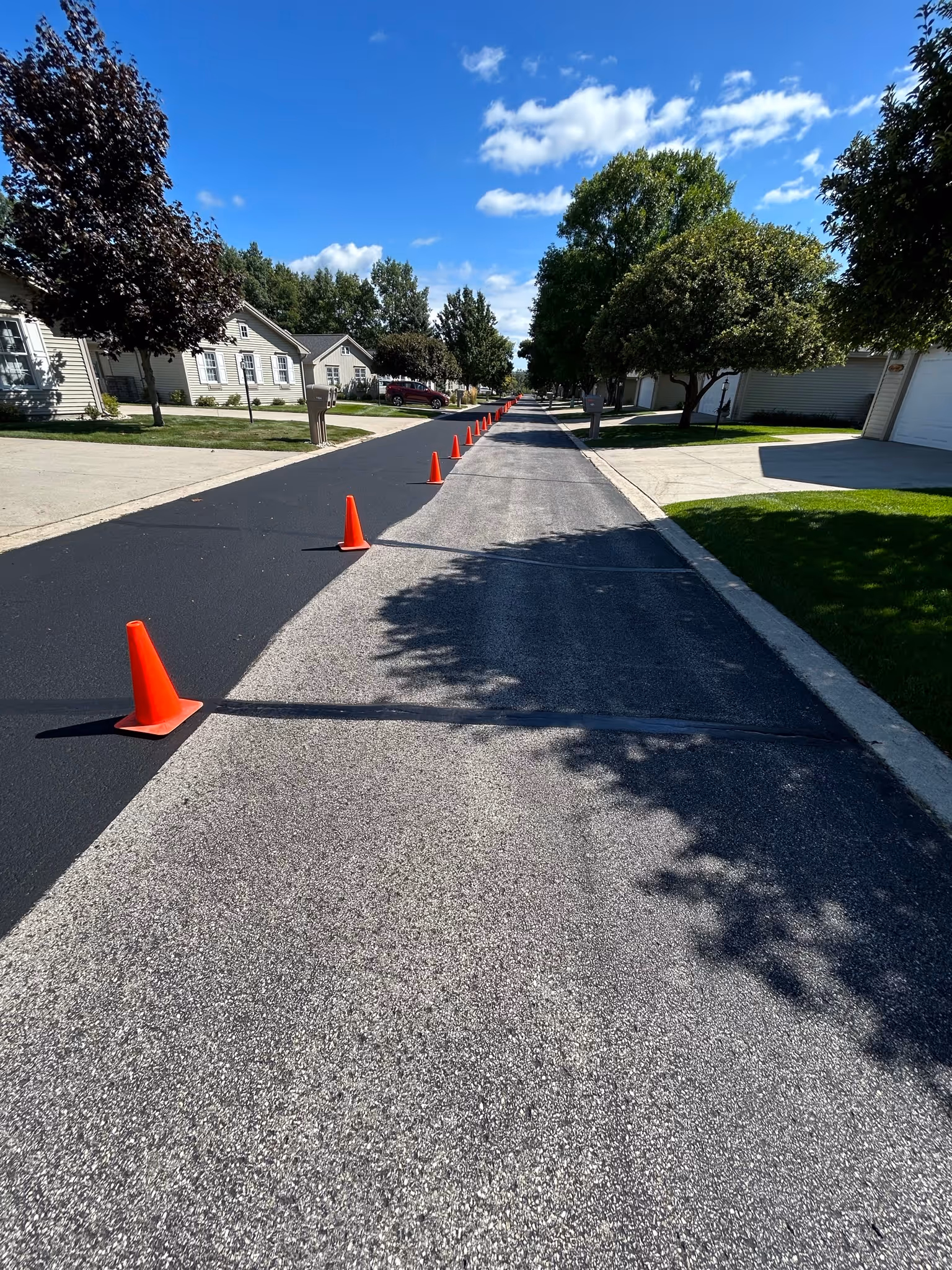 Professional HOA asphalt sealcoating at Garfield Condominiums on Hemingway Lane in Traverse City, MI, showcasing a fresh jet-black protective finish and phased lane application to maintain resident access.