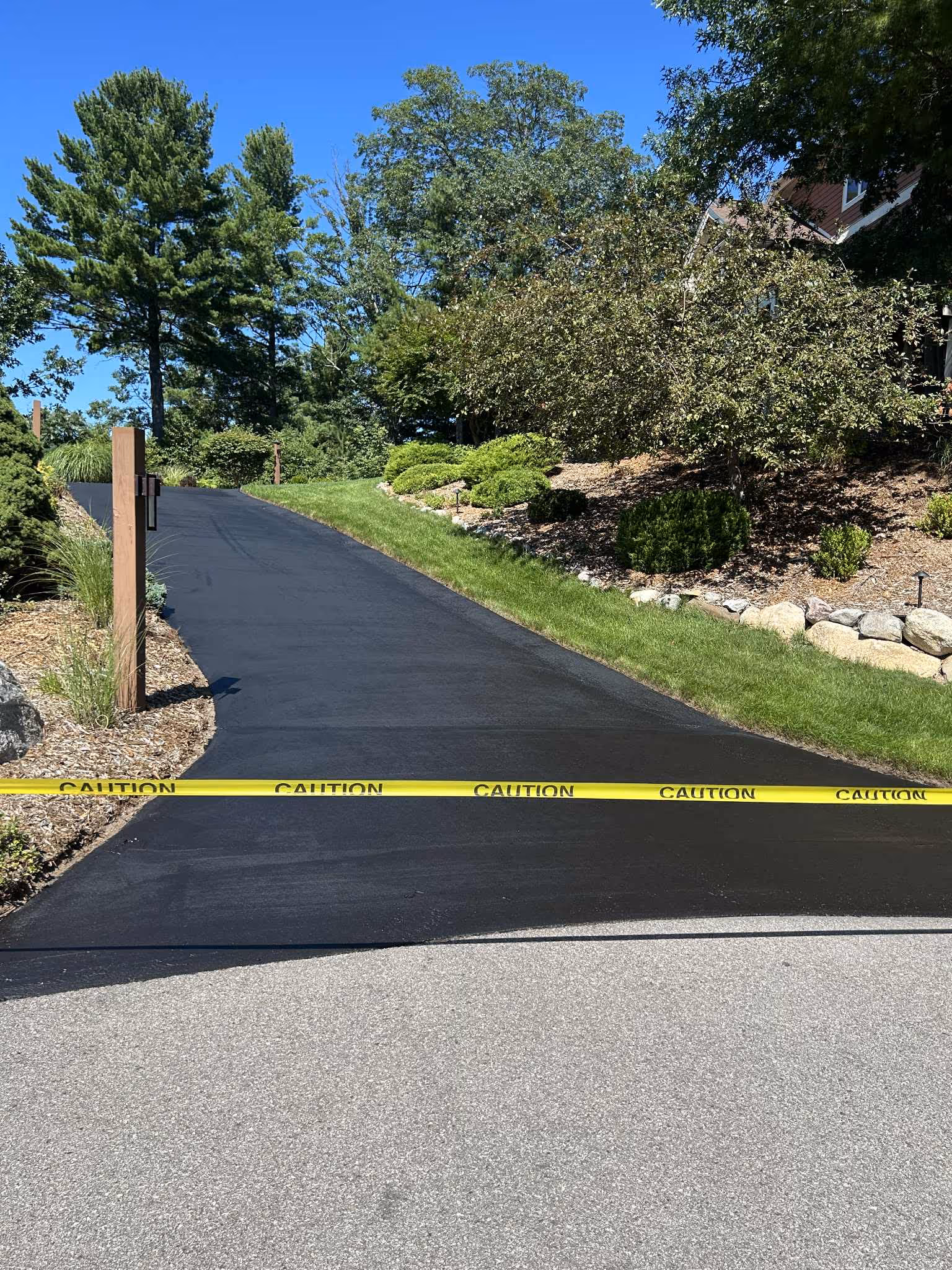 Professional residential asphalt sealcoating in Grand Traverse County, MI, showing a freshly applied jet-black finish protected by caution tape to ensure a perfect cure and long-lasting curb appeal.
