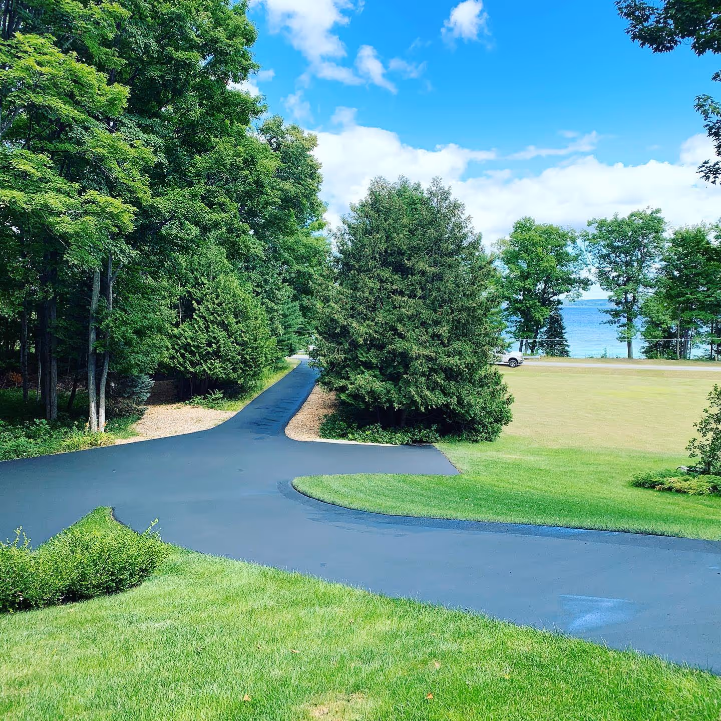 Freshly sealed asphalt driveway in a quiet Suttons Bay neighborhood featuring a jet-black finish.