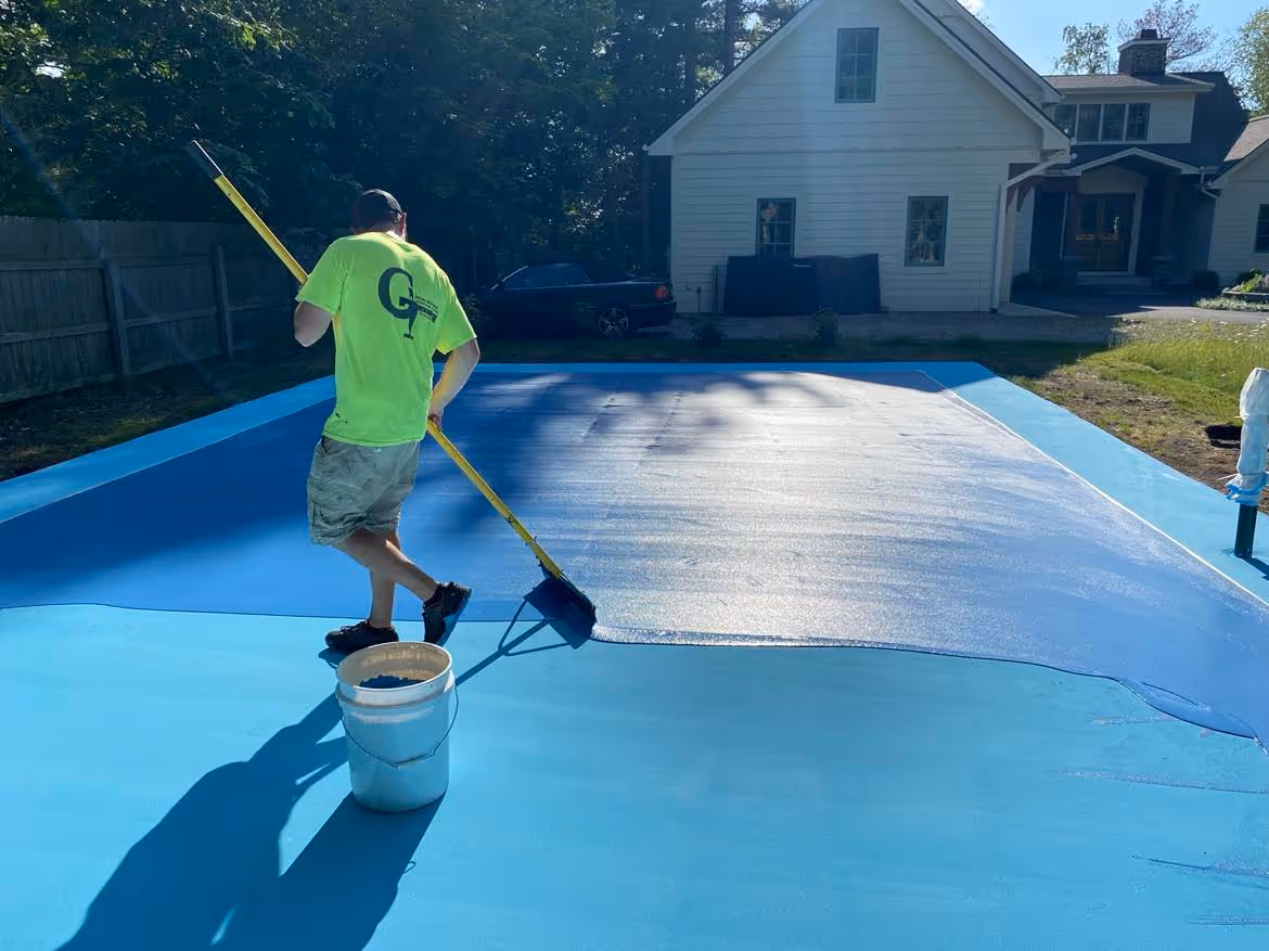 Professional crew member using a specialized squeegee applicator to apply the first vibrant textured color coat on a residential pickleball court in Bellaire.