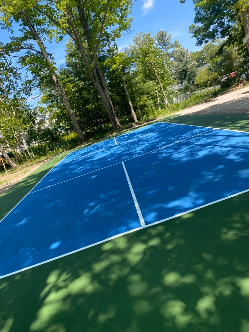The completed, professionally leveled and surfaced private pickleball court on Big Glen Lake in Glen Arbor, MI. The photo highlights the sharp two-tone blue and green finish with precision white line striping, ready for play.