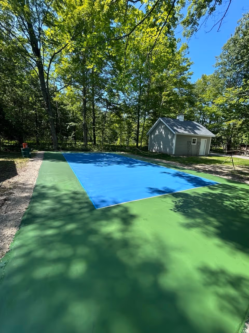 Application of the contrasting vibrant green SportMaster color coating to the out-of-bounds boundary area of the pickleball court on Dunns Farm Rd, defining the two-tone aesthetic.