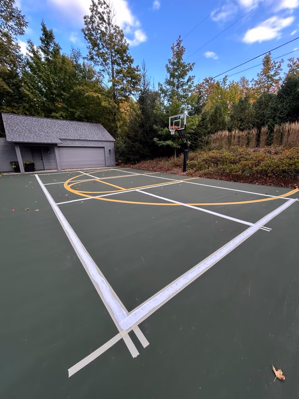 Painting the taped lines on the Elk Lake court—using bright white for pickleball and yellow for basketball—to ensure clear playability for both sports.