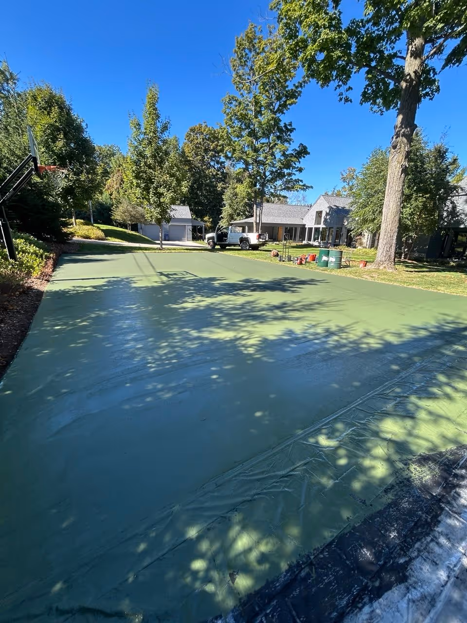 The second coat of vibrant green SportMaster acrylic color drying on the private court. The wet sheen shows the uniform application required for a professional-grade finish.
