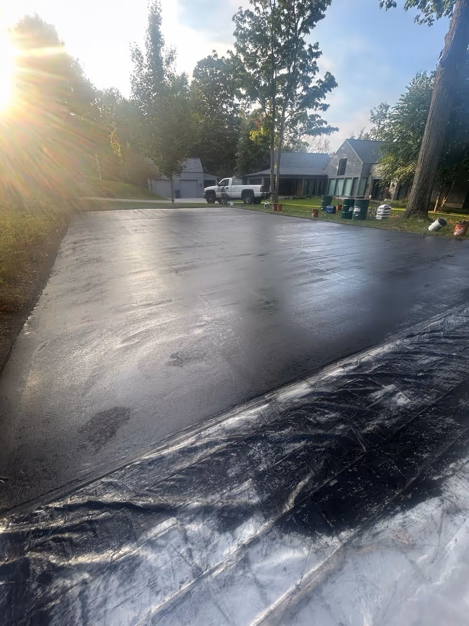 A layer of black SportMaster acrylic resurfacer drying on the Elk Lake court. This foundational coat fills the asphalt pores and levels the surface for the color layers.