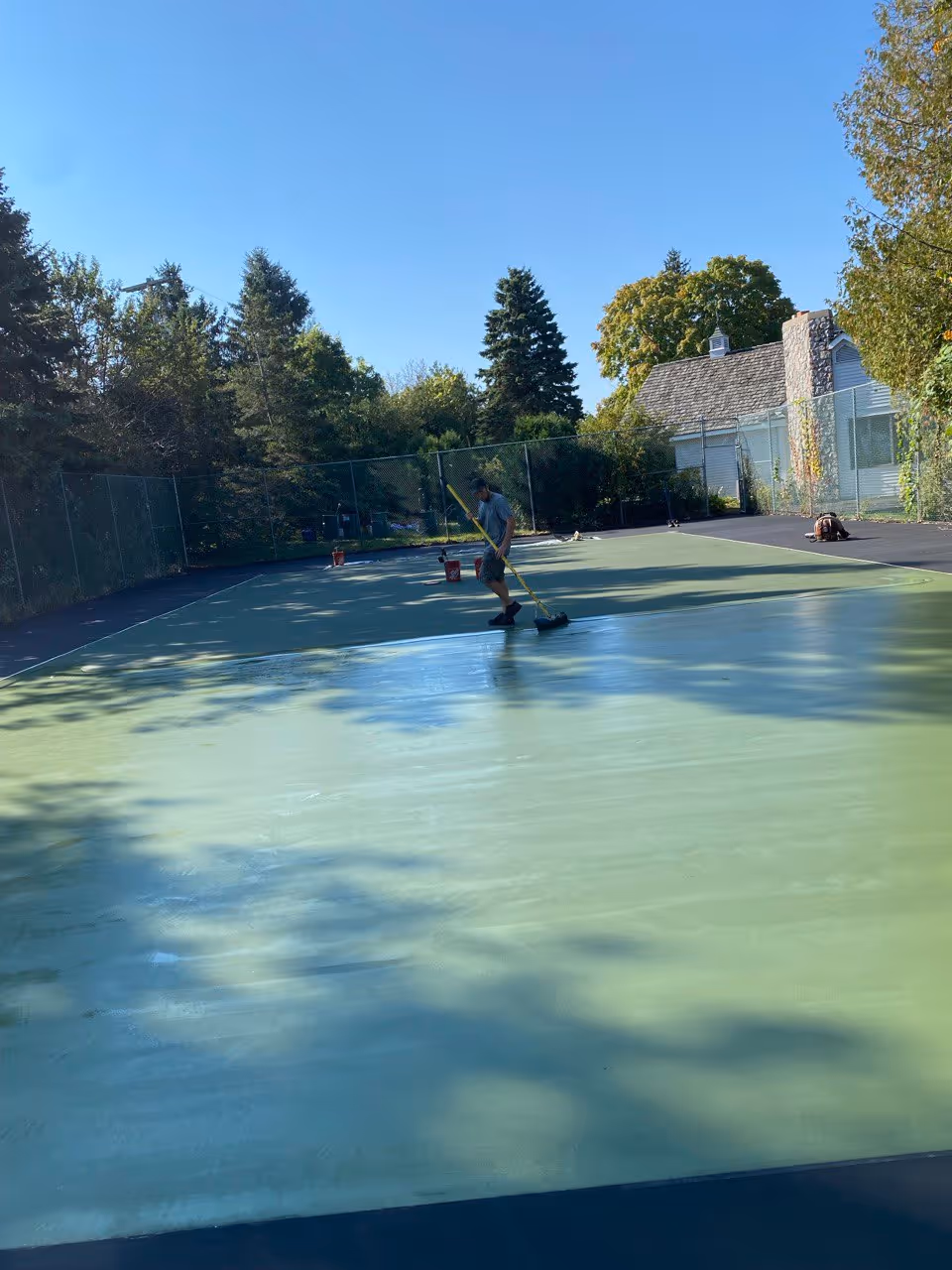 Professional workers applying the second coat of vibrant green SportMaster acrylic color to the interior of the Suttons Bay tennis court.