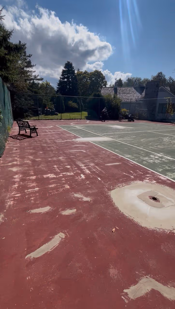A secondary view of the extensive repair work, showing filled cracks and leveled "birdbaths" across the tennis court surface on S Shore Dr.
