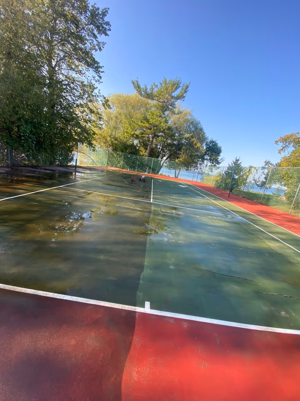 A dramatic progress shot showing half of the tennis court pressure washed, highlighting the massive difference in surface cleanliness and color restoration after removing years of oxidation.