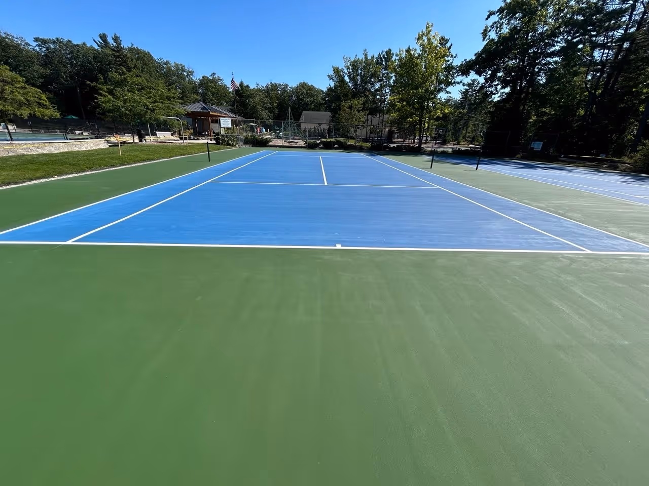 A view looking straight down the length of a newly surfaced tennis court at Glen Arbor Township Park, showing the crisp white lines and uniform texture of the high-performance coating.