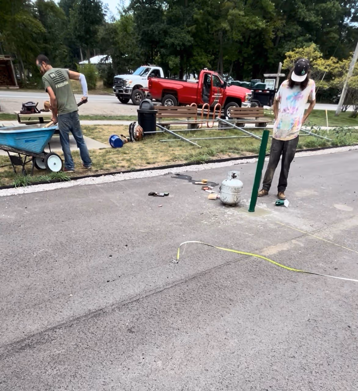 Two workers mixing and setting concrete to secure a new heavy-duty tennis net post into the new asphalt court at the Glen Arbor Township Park.