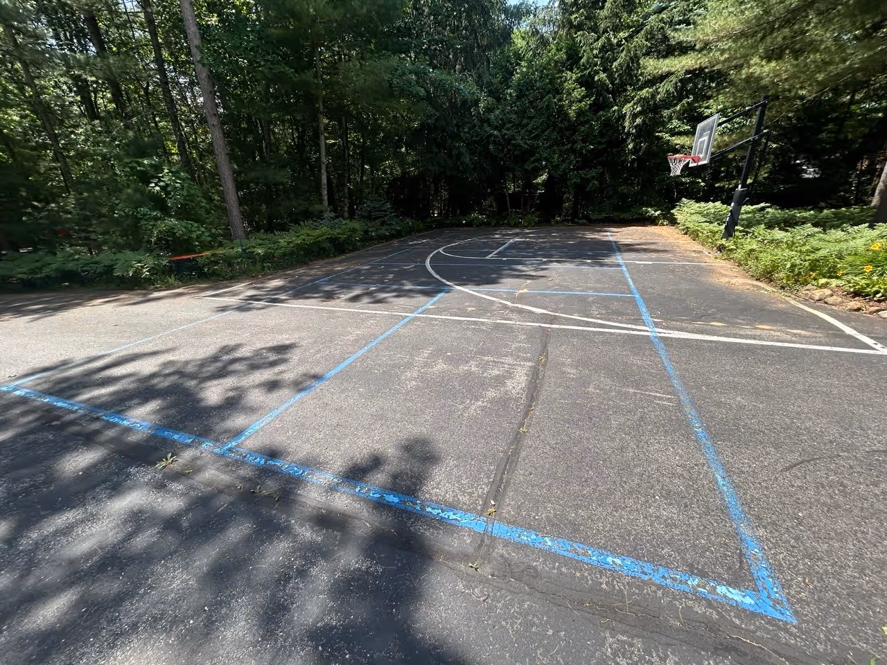 The "after" photo of the completed residential sealcoating project in Traverse City. The driveway on Long Lake has been restored with a rich black finish and features new, professional-grade blue pickleball and white basketball lines.