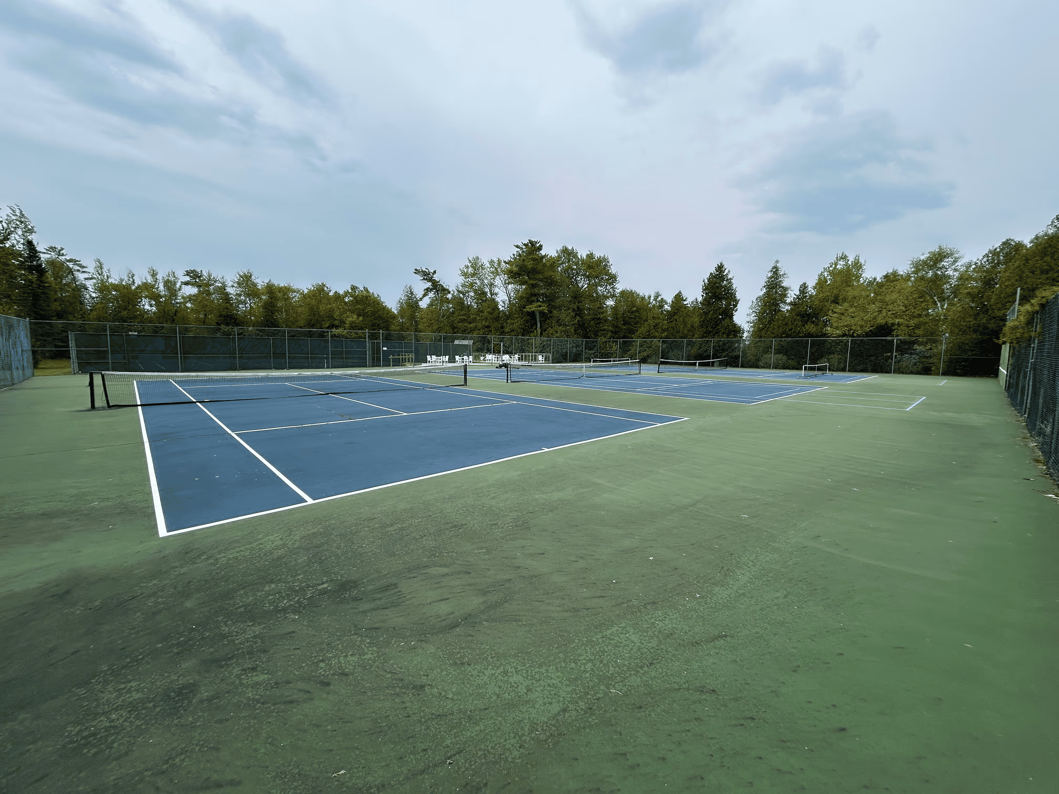 The original, faded, and deteriorated condition of the triple tennis courts at the Northport Point Homeowners Association before the start of the comprehensive restoration and pickleball conversion.