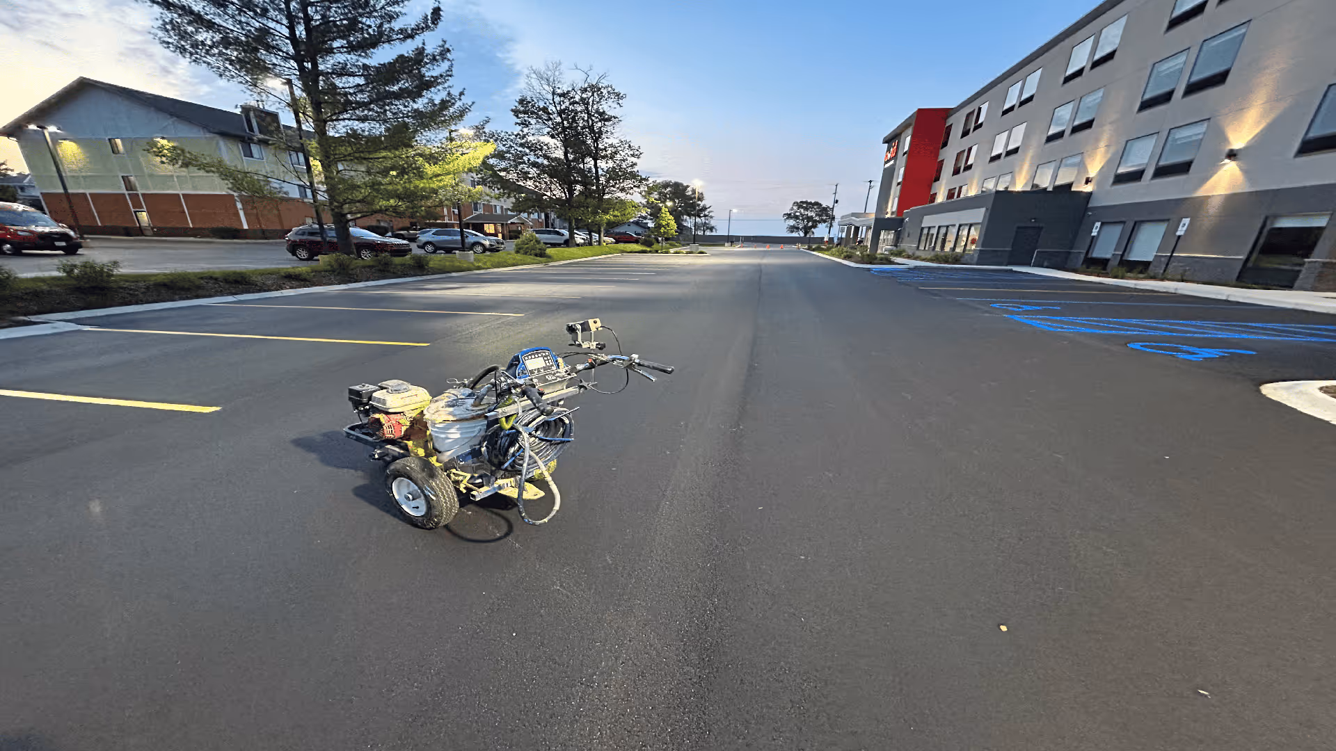 A new commercial parking lot layout and precision striping project at the Avid Hotel on US-31 in Traverse City, MI. The image shows a professional Graco striping machine in use during a collaborative project with Team Elmer's, ensuring crisp, high-visibility lines for the new hotel facility.