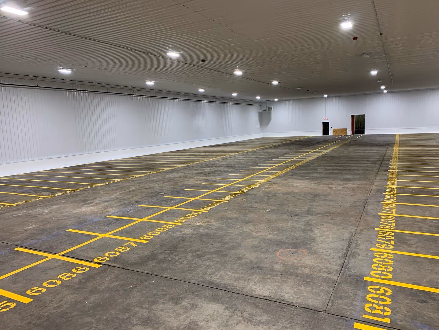 Professional interior concrete line striping and pallet storage numbering at the Gogo Squeez facility in Grawn, MI. This industrial warehouse layout project, completed for Grand Traverse Construction, features precision-striped lanes and numerical organizational markings for efficient logistics and storage.
