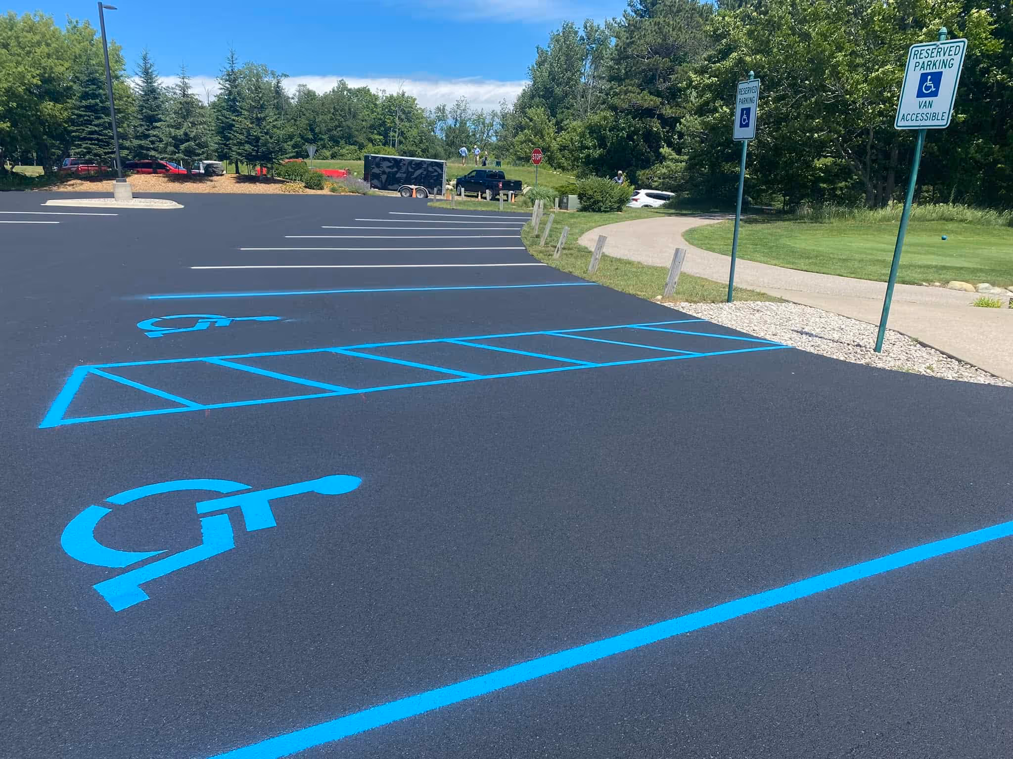 A professionally sealed and re-striped parking lot at Northport Creek Golf Course in Northport, MI. The image features a fresh, deep black asphalt finish with high-visibility yellow parking lines and ADA-compliant blue handicap stalls, ensuring safety and accessibility for golfers and guests.