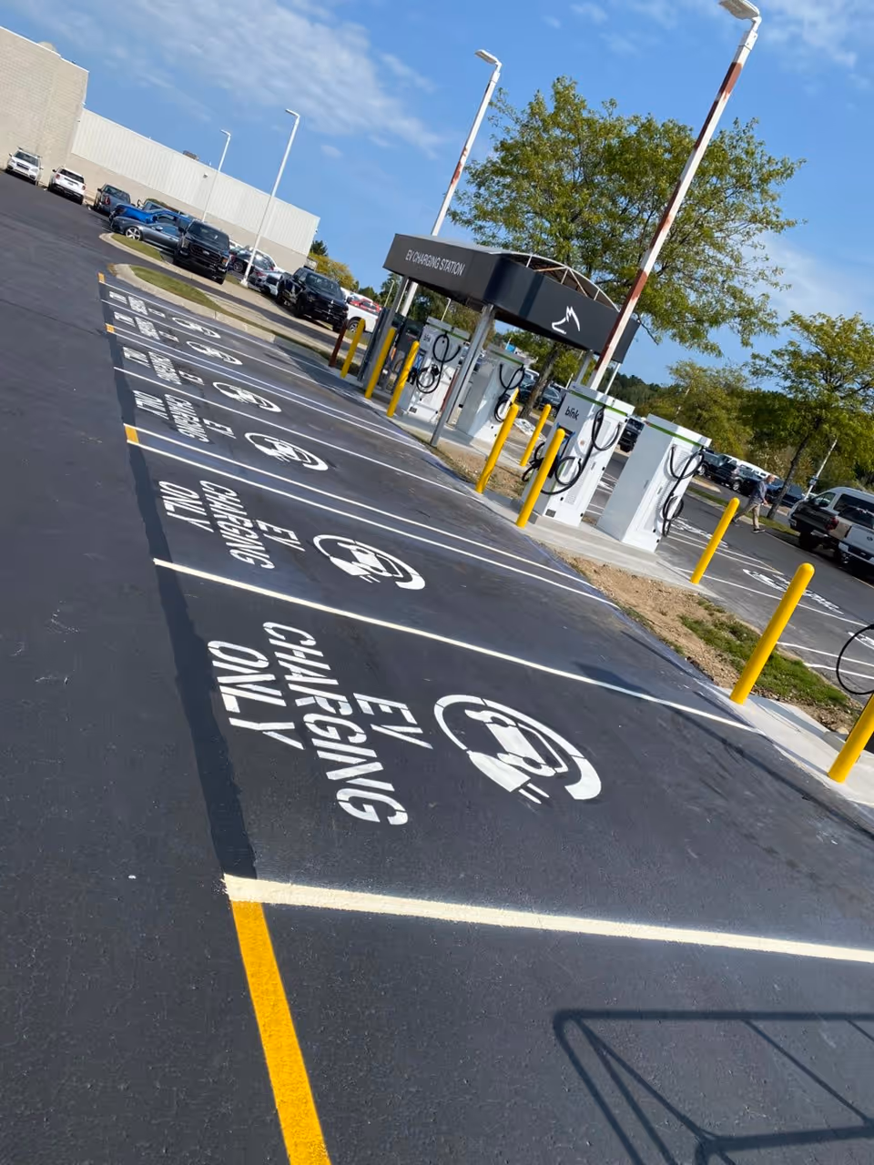 A specialized EV charging station layout and precision pavement markings at Fox Grand Traverse Ford on N US-31 S in Traverse City, MI. Completed in collaboration with R W Mercer Co, the project features vibrant green and white electric vehicle (EV) only symbols and stall striping on fresh asphalt.