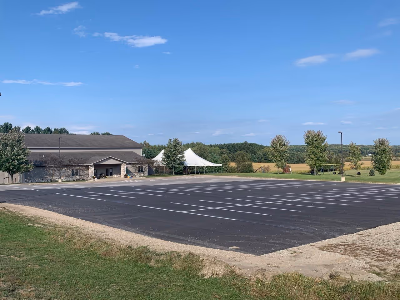 A newly paved asphalt parking lot at the Revival Center of Cadillac on M-55 in Cadillac, MI. The image showcases a precision-engineered new layout with crisp white line striping, providing organized parking and high-visibility pavement markings for the community worship center.