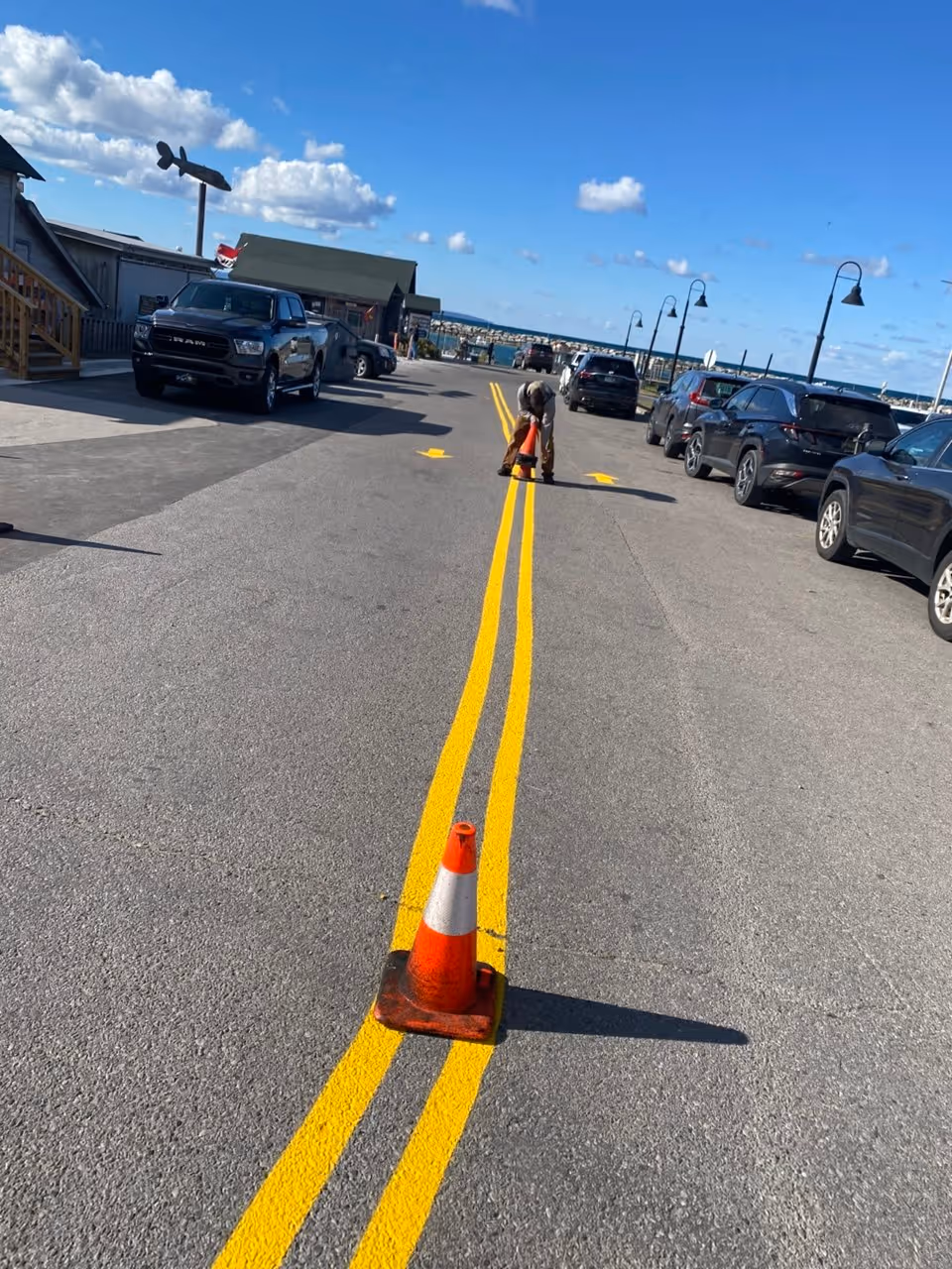 A new road layout and precision line striping project at Fishtown in Leland, MI. The image shows freshly applied high-visibility double yellow centerlines and directional white arrows on new asphalt, completed for Team Elmer's to optimize traffic flow and safety near the historic Leland harbor.