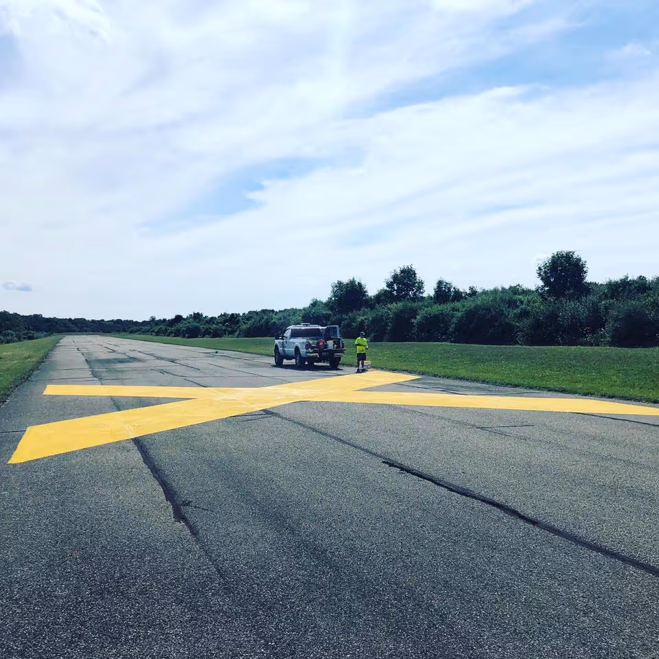 Specialized airfield pavement markings applied at the Wallace G. Fryer Airfield (Sugar Loaf) on E Mountain Rd in Cedar, MI. The image shows the precision application of large runway closure symbols, demonstrating high-level expertise in aviation-grade striping and airfield decommissioning protocols.