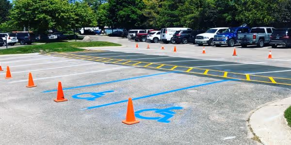 A new parking lot layout and precision striping at Harbor West Yacht Club on the Pure Michigan Byway M-22 in Traverse City, MI. The image features crisp white parking stalls, ADA-compliant blue handicap stalls with international symbols, and a vibrant yellow walkway cross-hatch to ensure pedestrian safety for club members and maritime guests.