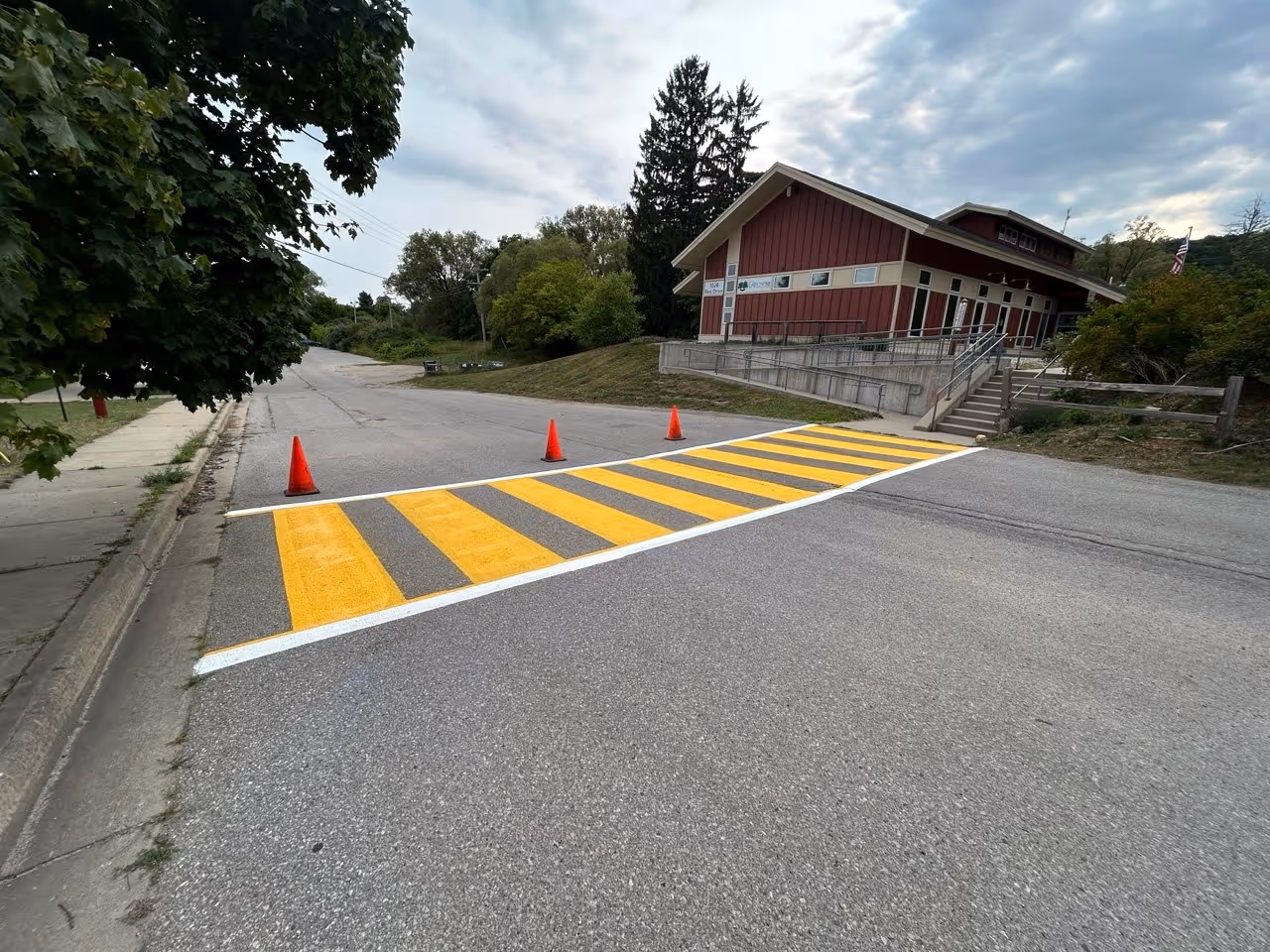 A new precision-engineered crosswalk layout and line striping project in high-visibility white and yellow paint at The Greenspire School in Traverse City, MI. The image highlights active site safety with orange cones directing traffic and blocking the road to ensure a professional and safe installation of pedestrian pavement markings.