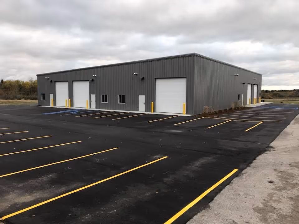 A new parking lot layout and precision striping at Koala Insulation on Industrial Circle in Traverse City, MI. The image features vibrant yellow and blue pavement markings on freshly laid asphalt, highlighting professional traffic organization and ADA-compliant stalls for this local industrial service provider.