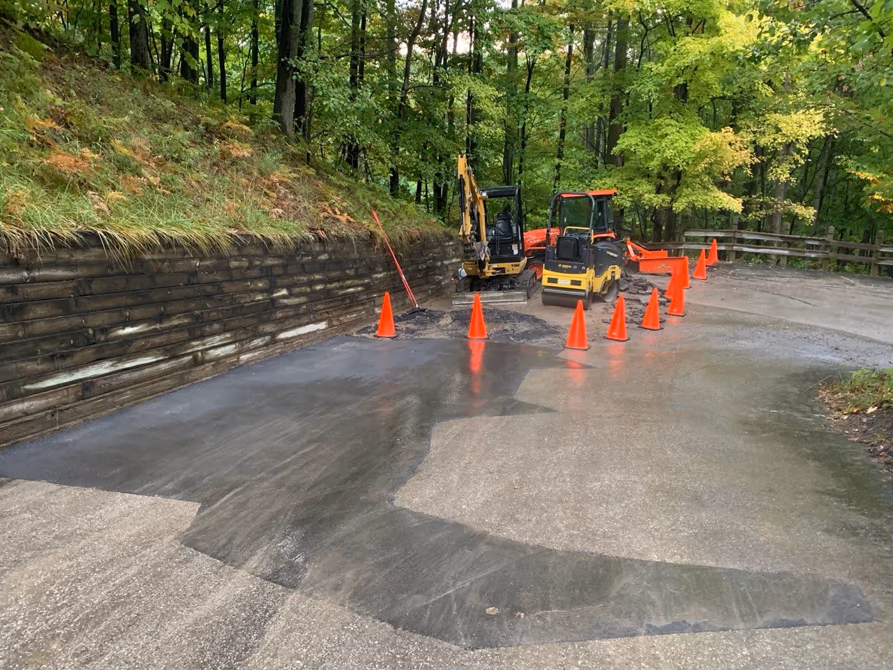A completed asphalt patch on the main drive of Pinnacle Place at The Homestead Resort. The orange safety cones and Caterpillar mini-excavator have moved down the hill to the next repair section, showing systematic progress on the private road.