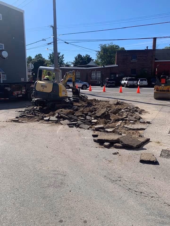 A Wacker Neuson mini rubber-tracked excavator removing damaged asphalt at the Rare Bird Brewpub parking lot. This "cut and replace" method ensures the complete removal of failed sub-base materials before new asphalt is installed.