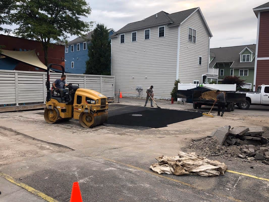 Professional asphalt crew raking hot-mix asphalt at Rare Bird Brewpub while a Caterpillar asphalt roller compacts the new surface for maximum durability and a smooth finish in the downtown Traverse City parking lot.