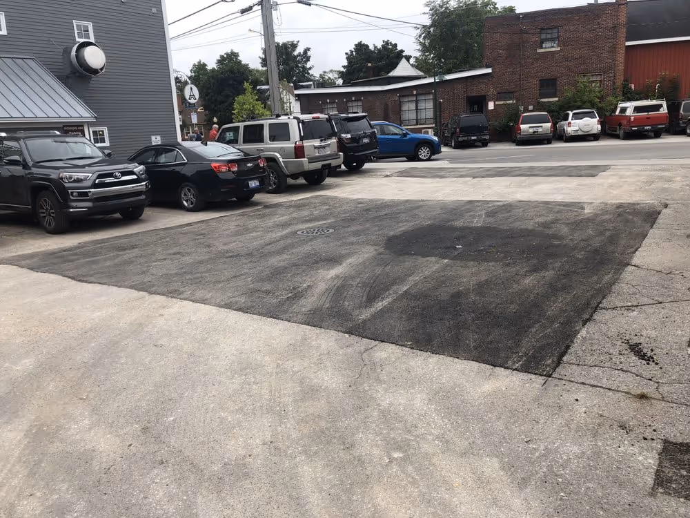 The first completed asphalt patch at Rare Bird Brewpub, showing a flush, professional repair. The parking lot area is reopened to patrons, demonstrating a quick turnaround for a busy Traverse City business.