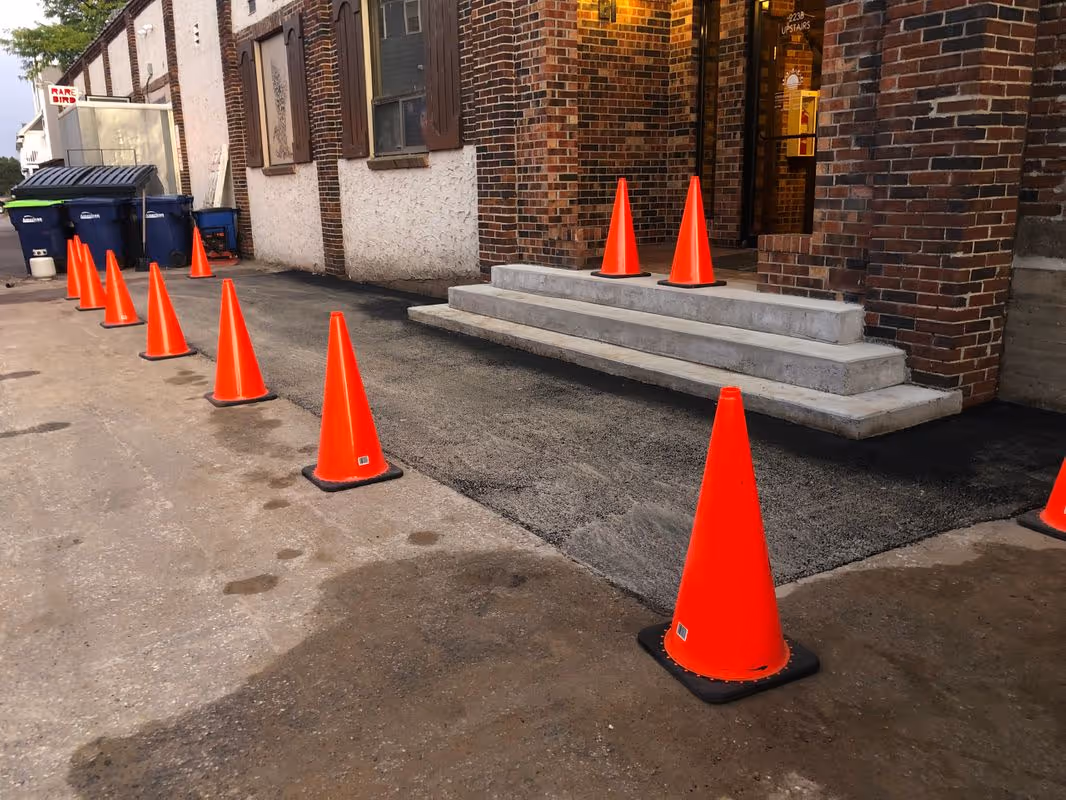 Fresh hot-mix asphalt installed and rolled at the Rare Bird Brewpub entrance. Orange traffic cones protect the newly paved area, allowing the material to set properly before being exposed to vehicle traffic.