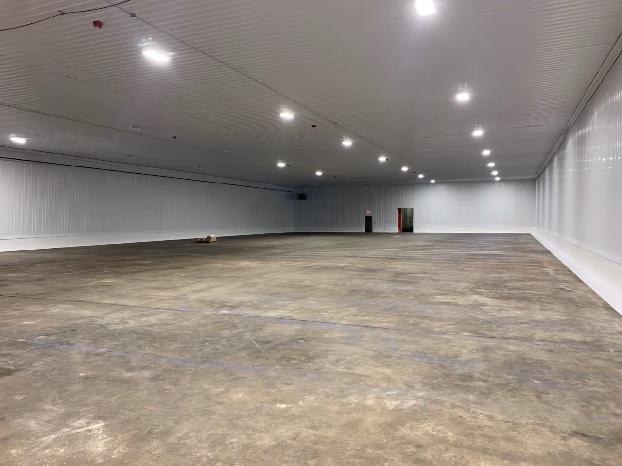 A bare interior concrete warehouse floor at the GoGo SqueeZ facility in Grawn, MI, prior to professional pallet striping. This "before" image shows the clean industrial concrete slab prepared for high-precision logistics layout and storage numbering for Grand Traverse Construction.