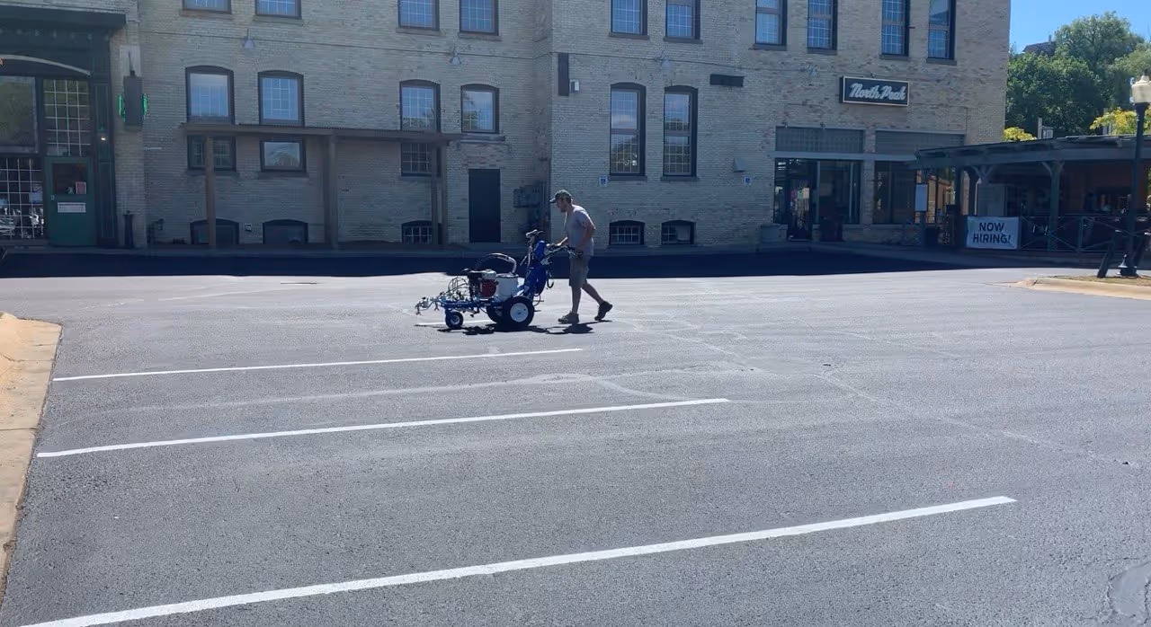 Precision parking lot striping at North Peak Brewing Company in Traverse City. A worker uses a Graco LineLazer 3900 to paint crisp white lines on freshly repaired and sealed asphalt, restoring the professional appearance of the downtown landmark.