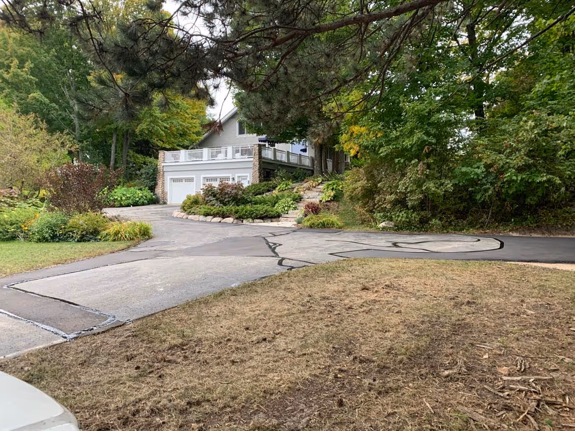 The completed residential driveway repair project in Suttons Bay, MI. All patches are finished with professional hot rubber crack sealer applied to the seams between new and existing asphalt, providing a water-tight, high-durability finish on N West Bayshore Dr.
