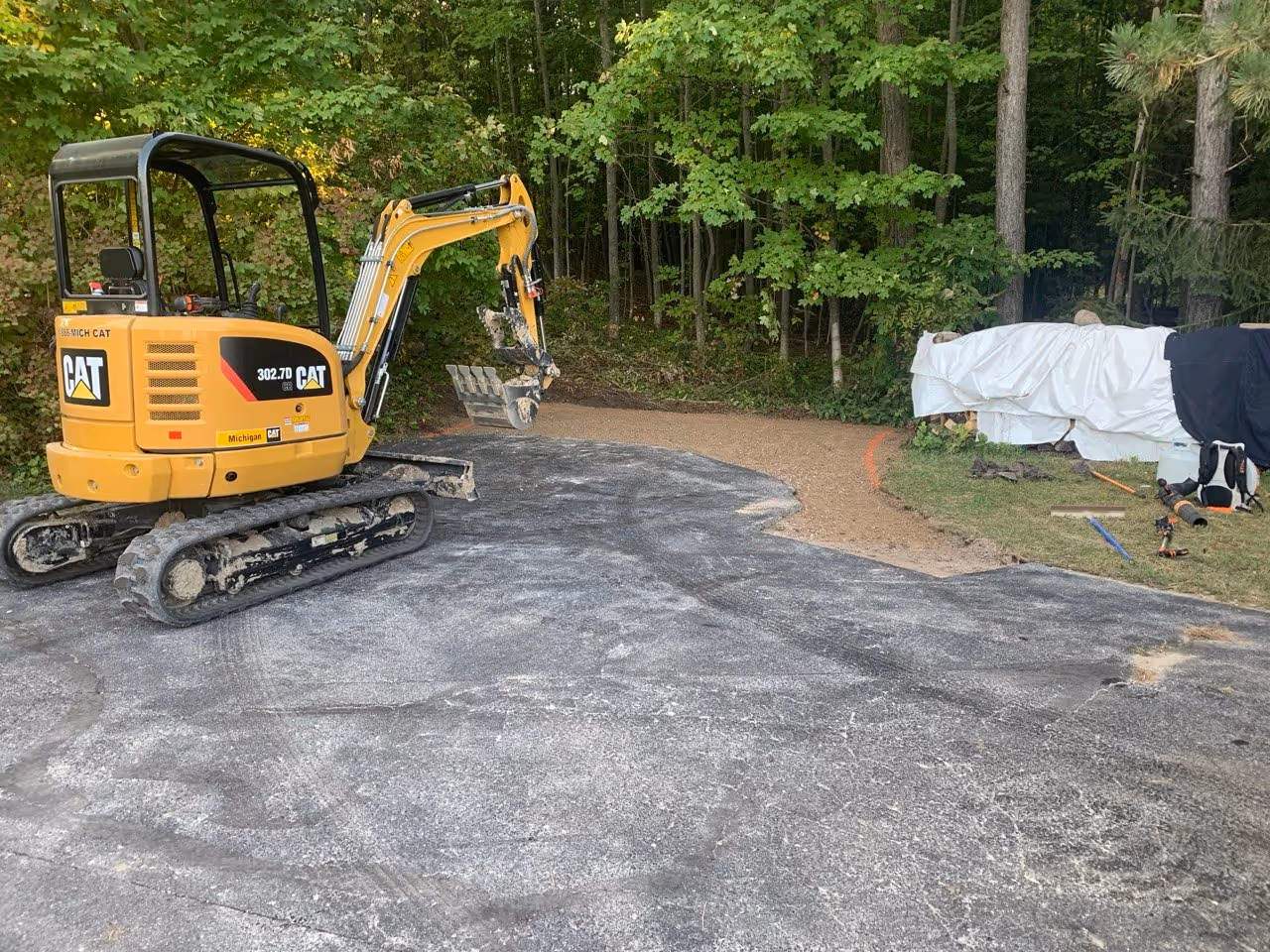 Structural base preparation for a Suttons Bay driveway repair. A Caterpillar 302.7D rubber-tracked excavator installs and grades 22A road gravel to ensure a stable, long-lasting foundation for the new asphalt patches.