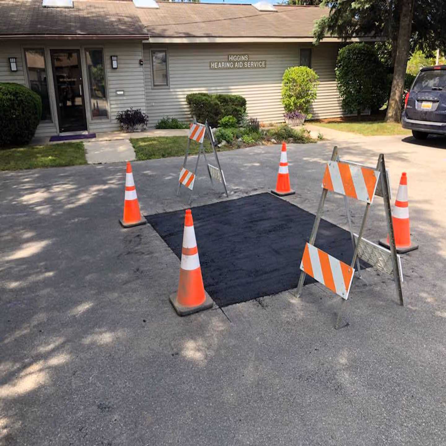 A finished and compacted asphalt patch at the W Front St clinic. The repair area is secured with safety cones to allow the new asphalt to cure, demonstrating a flush and level surface restoration.