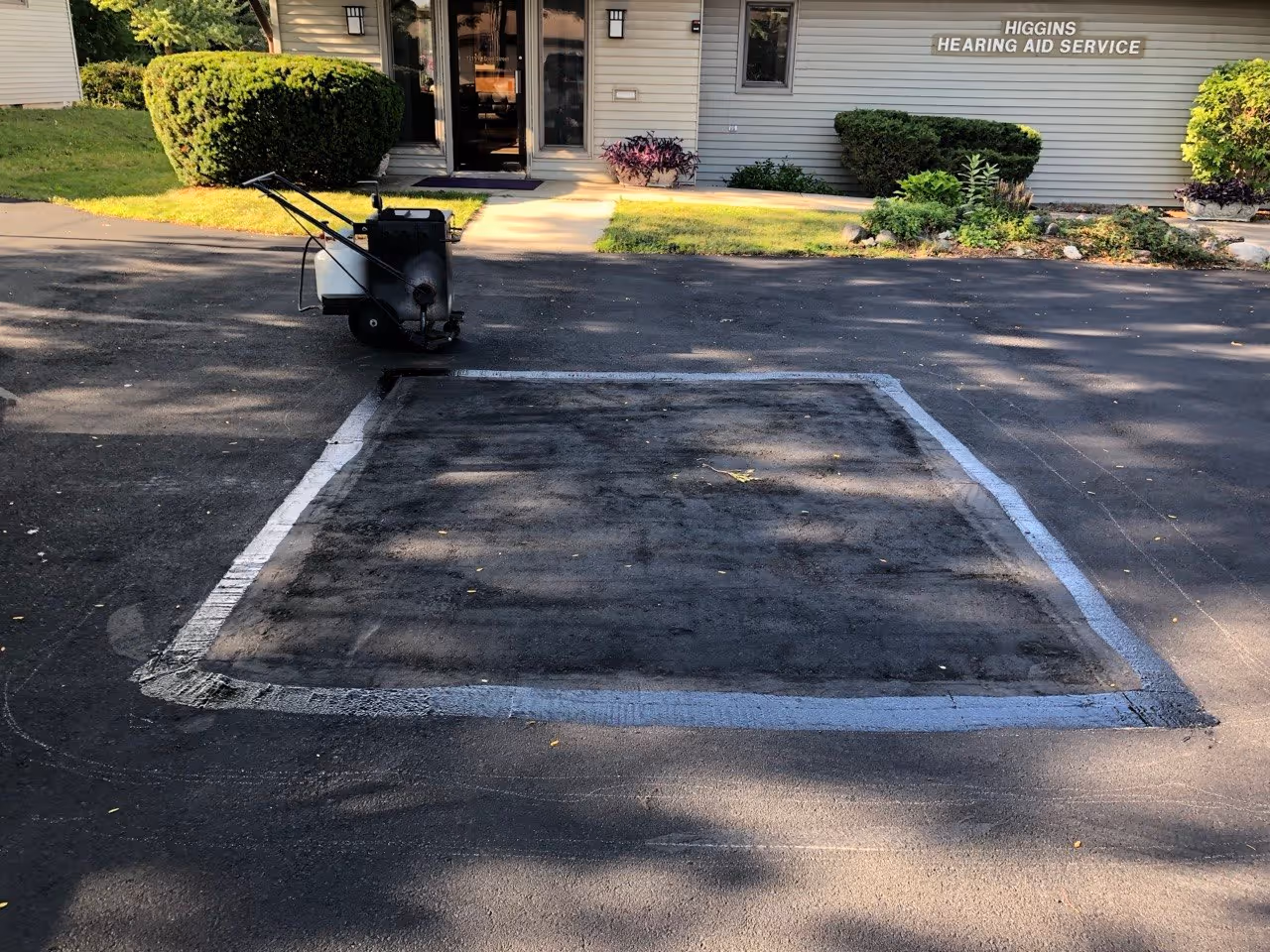 Perimeter waterproofing of a new asphalt patch using 380-degree Deery crack filler. A Gingway MA10 wheeled crack sealer melter is visible in the background, ensuring a water-tight bond between the new and existing pavement.