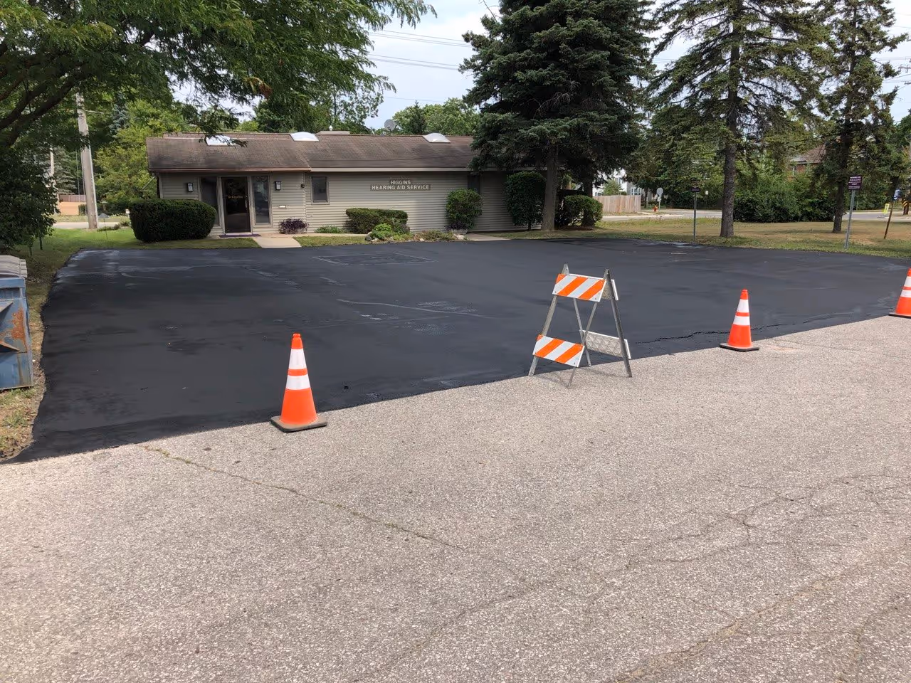 The completed parking lot at Higgins Hearing and Audiology in Traverse City, MI. The surface is freshly sealcoated and coned off, representing a full restoration of the commercial property's curb appeal and durability.