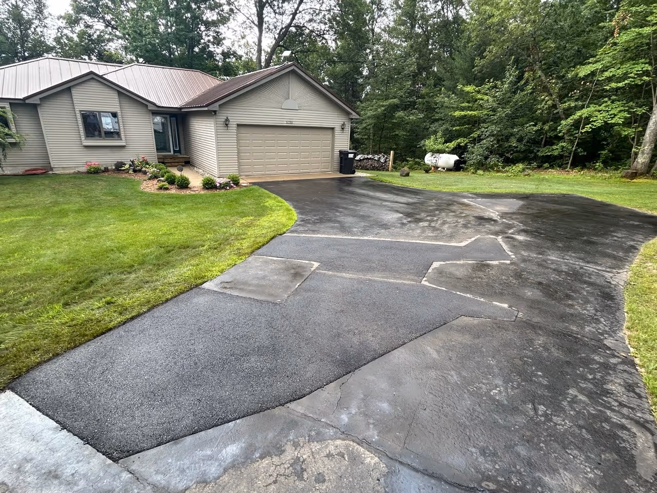 A professionally completed residential driveway asphalt repair on Supply Rd in Traverse City, MI. The image showcases a smooth, structural cut-and-replace patch that has been precisely compacted and finished to provide a level, durable surface for the homeowner.