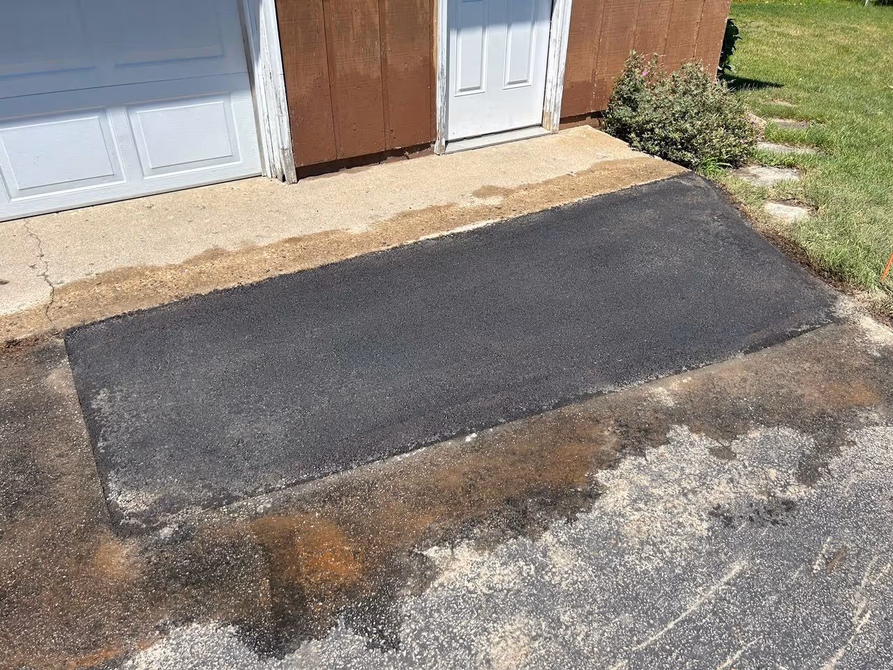 A precision residential asphalt driveway repair at the corner of Sandia Place and Vista Park in Traverse City, MI. The image showcases a seamless, structural patch where the concrete garage apron meets the new asphalt, ensuring a smooth transition and proper drainage for a home in the subdivision off Veterans Dr.