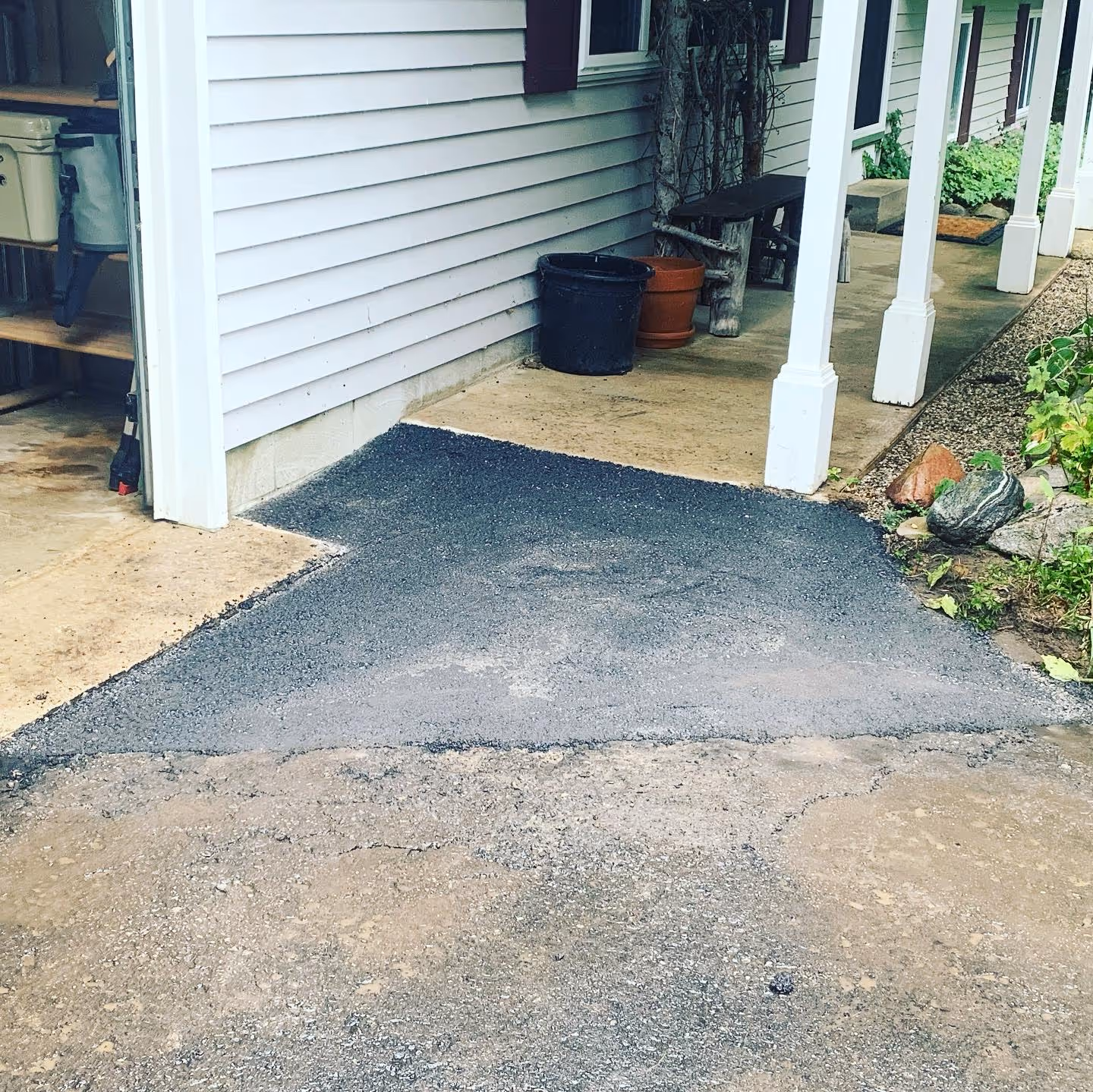 A residential asphalt driveway repair and addition on Minkin Dr in Traverse City, MI. The image displays new asphalt perfectly integrated with a concrete garage apron and sloped to meet a raised front porch sidewalk, providing a seamless transition for a home in the subdivision between W Long Lake Rd and Fisher Rd.