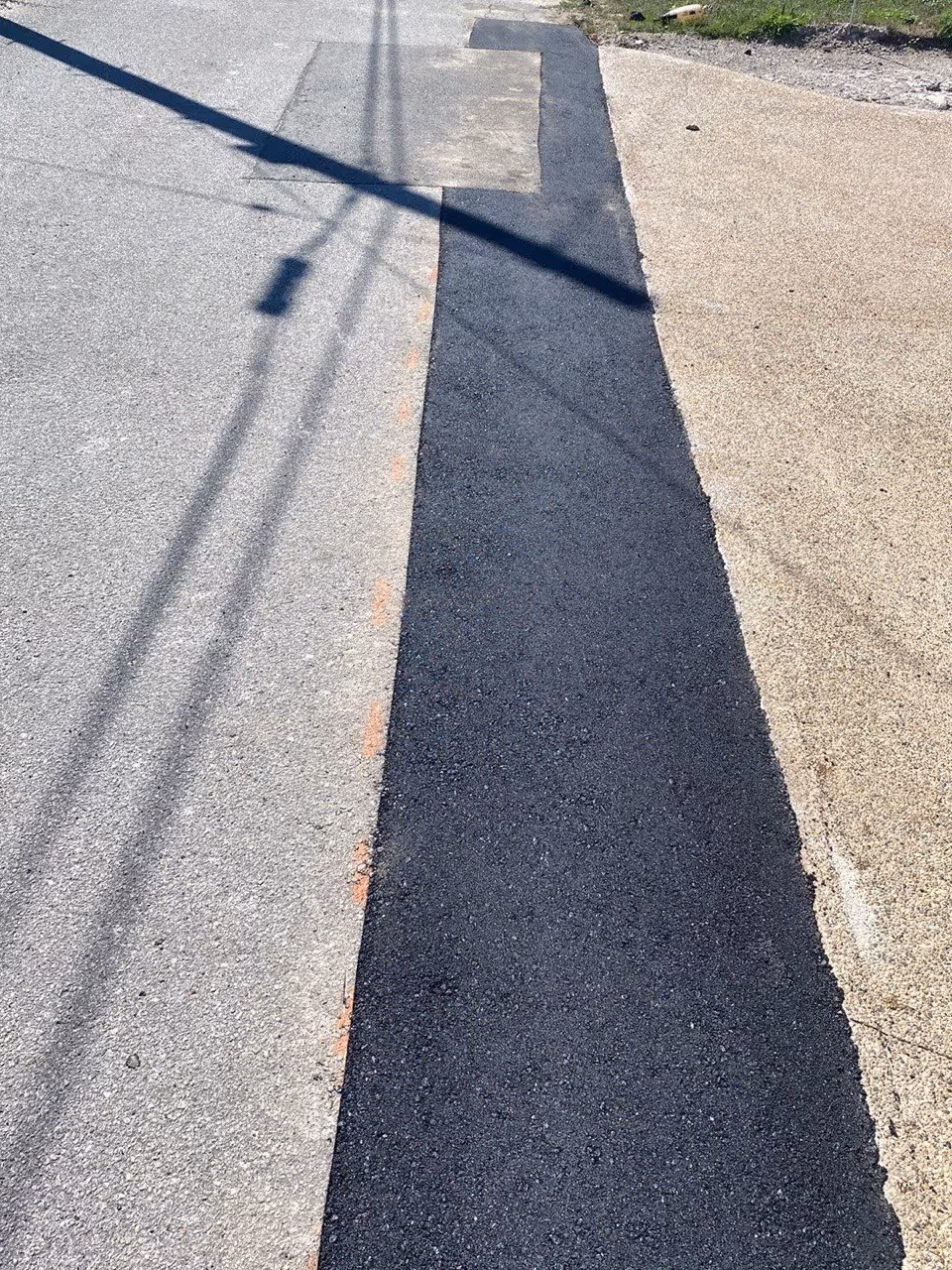 A professional cut and replace asphalt repair on a failing section of road adjoining a residential concrete driveway in downtown Frankfort, Michigan. The image shows the new, smooth-compacted asphalt strip providing a durable and level transition between the city street and the private concrete entrance.