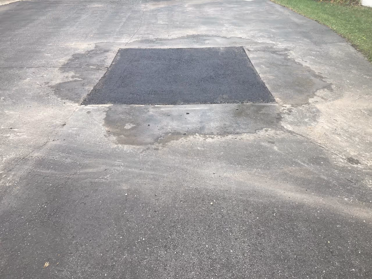 A professionally installed large square asphalt repair patch on a residential driveway on Washington St in Traverse City, MI. This structural patch specifically addresses a low spot to prevent water pooling and improve drainage, restoring a level and durable surface for a home in the historic downtown district.