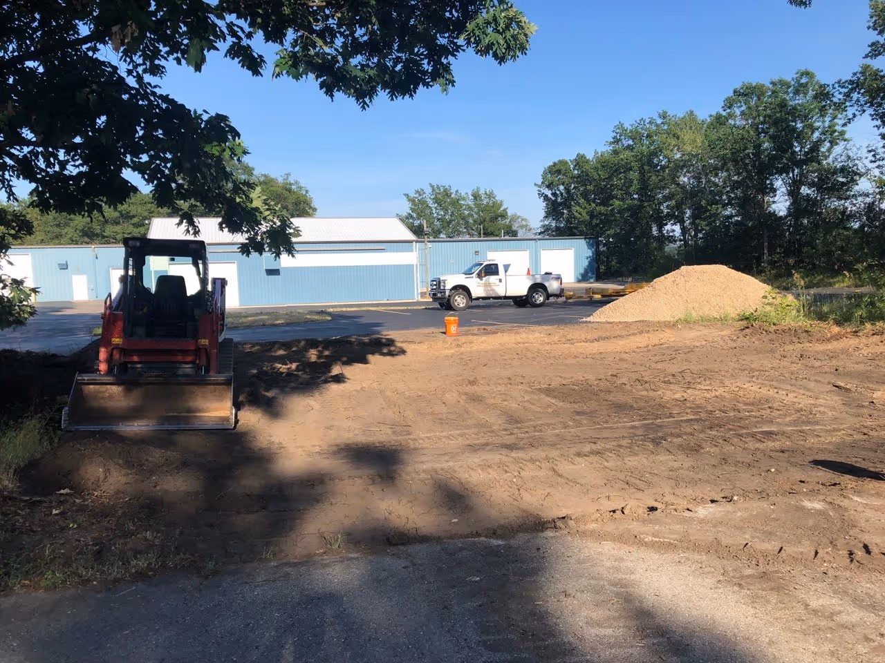 Spreading 22A road gravel for a stable aggregate base at the Hagerty Insurance commercial parking lot connection. A skid steer ensures even distribution of the foundation material to prevent future asphalt shifting or cracking.