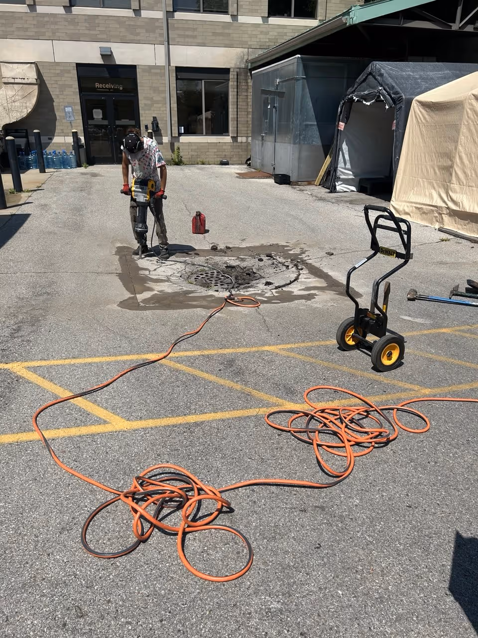 A professional pavement restoration worker using a jackhammer to remove asphalt and concrete around a failed catch basin driveway drain in Northern Michigan.